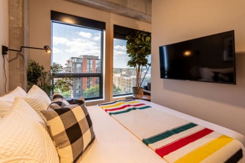 Modern bedroom featuring colorful blanket, pillows, and urban view outside the window.