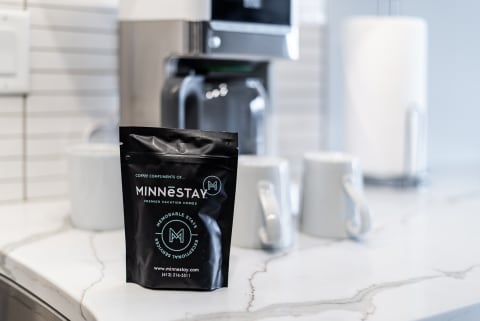 A packet of coffee from MINNēSTAY on a marble kitchen countertop with white mugs in the background.