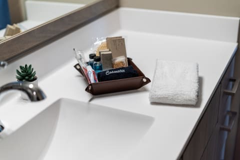 Modern bathroom countertop featuring toiletries in a tray, a potted plant, and a white towel.