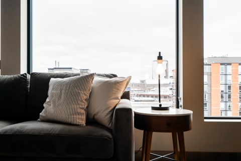 Cozy living room with a gray couch and a lamp, overlooking a cityscape.