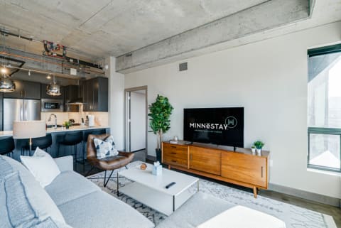 Modern living room with gray sofa, wooden TV stand, and kitchen in the background.