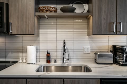 Contemporary kitchen countertop with stainless steel sink, paper towel holder, and kitchen appliances.