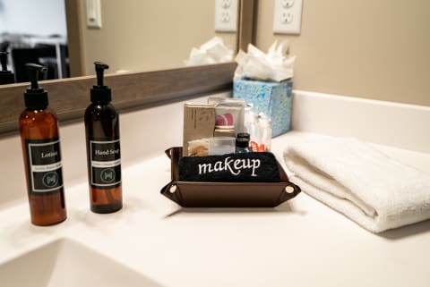 A bathroom countertop featuring lotion, hand soap, an organized makeup area, and a folded towel.