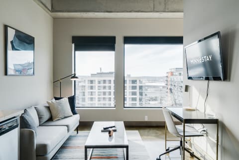 Interior of a modern living space featuring a gray sofa, large windows, and a work desk.