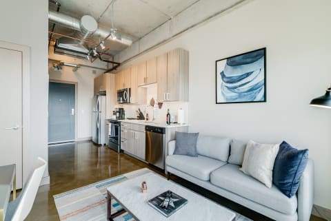 An open-concept apartment with a kitchen and living area featuring a light gray sofa and contemporary decor.