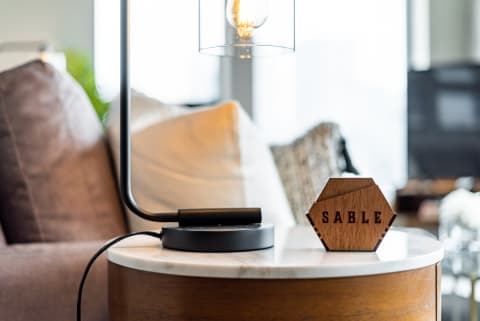 Close-up of a modern lamp and a wooden piece with the word SABLE on a marble table.