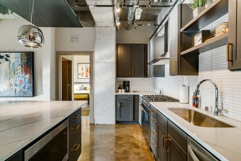 Contemporary kitchen with dark cabinets, white countertops, and a view into a living area.