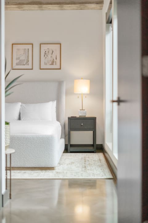 Modern bedroom with a white bed, nightstand, and abstract art on the walls.