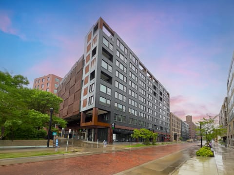 A modern urban building with a mixed material facade and a wet street reflecting the sky.