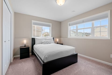 Cozy bedroom with a bed, nightstands, and large windows showcasing a neighborhood view.
