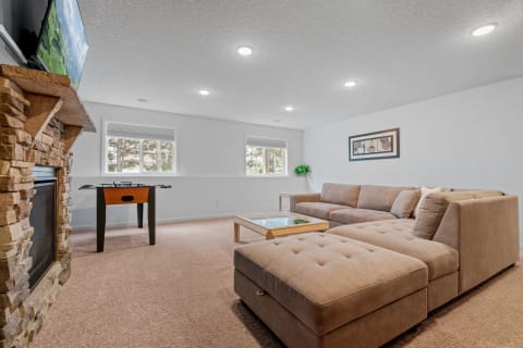 A living room with a sectional sofa, foosball table, and stone fireplace.