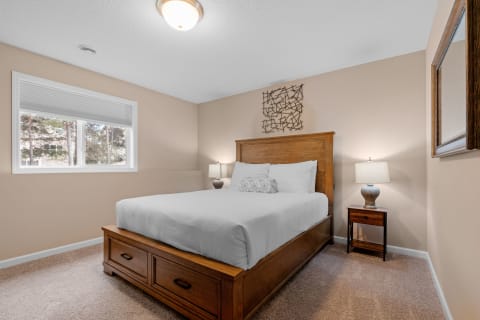 A cozy bedroom with a wooden bed, beige walls, and a window overlooking greenery.