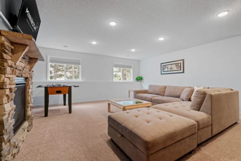 Cozy living room featuring a sectional sofa, foosball table, stone fireplace, and natural light from windows.