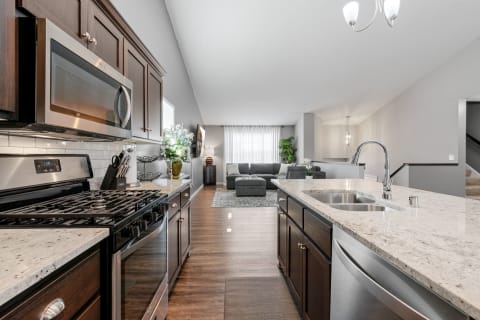 A modern kitchen with dark cabinets and granite countertops, leading into a cozy gray living room.