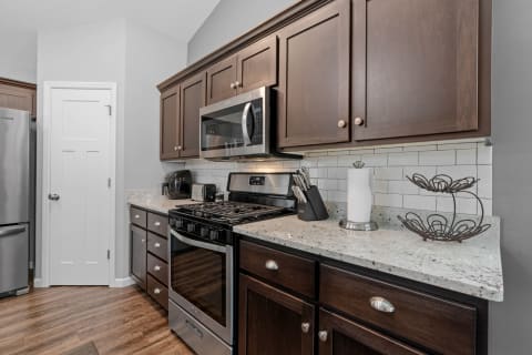 Contemporary kitchen featuring dark wooden cabinets, a stainless steel stove and microwave, and light granite countertops.