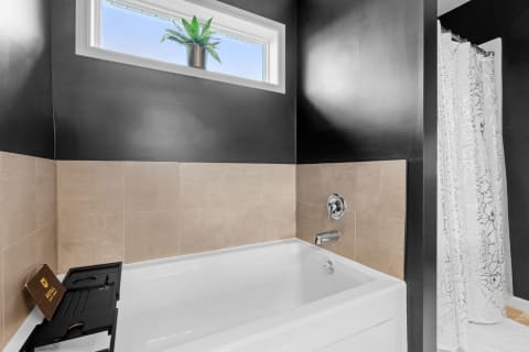 Modern bathroom with a white bathtub, black and beige walls, and a potted plant near a window.