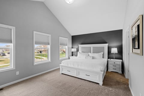 A bright bedroom featuring a large white bed, gray walls, and two windows.
