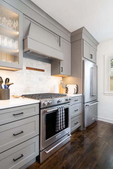 A modern kitchen featuring gray cabinets, a stainless steel range, and a marble backsplash.