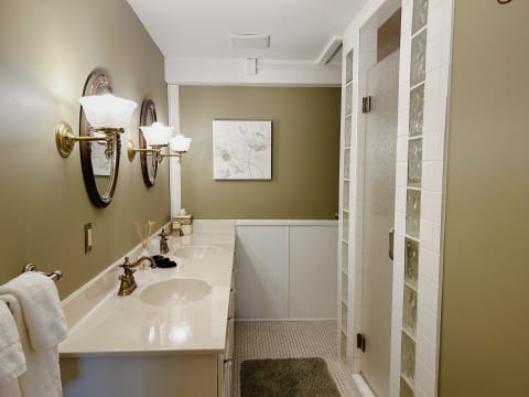 An elegant bathroom with a marble countertop, dual sinks, decorative lighting, and a glass-enclosed shower.