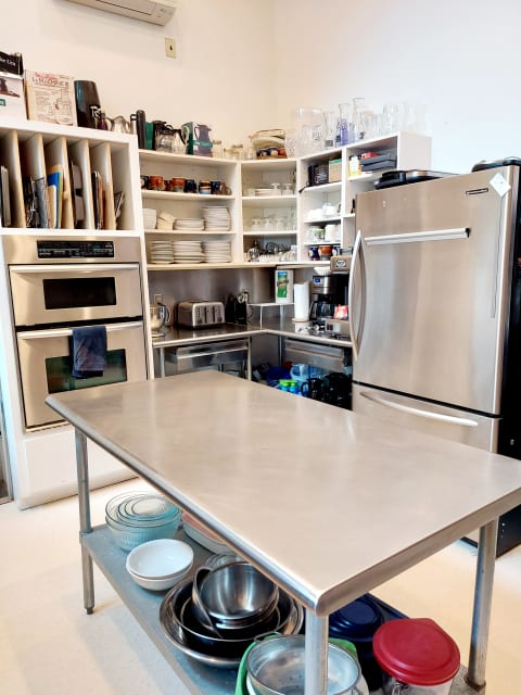 A fully equipped kitchen with a stainless steel countertop, modern appliances, and organized shelves of kitchenware.