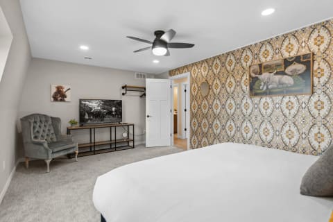 A beautifully designed bedroom featuring a white bed, vintage wallpaper, and a flat-screen TV.
