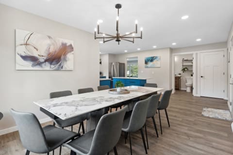 Modern dining area with a marble dining table, gray chairs, and a blue kitchen in the background.