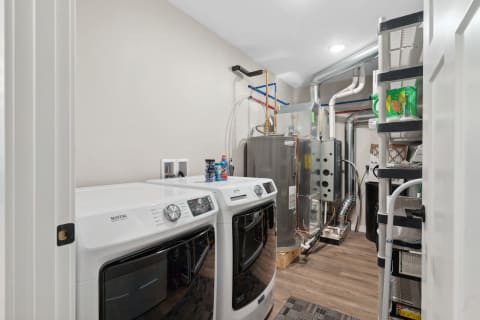 A well-arranged laundry room with Maytag washing and drying machines, a water heater, and storage shelves.