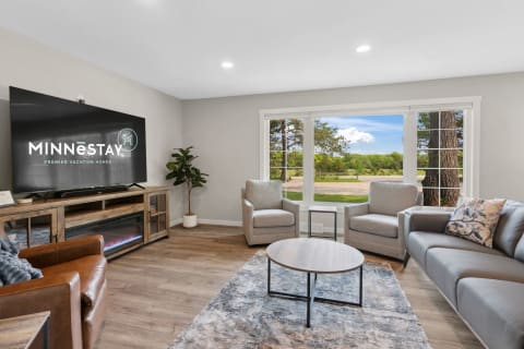 A modern living room with a large TV, stylish furniture, and a view of greenery through the window.