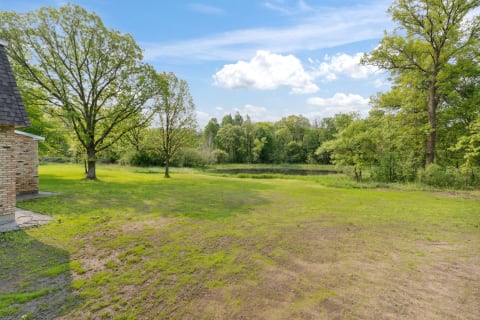 Scenic landscape featuring grass, trees, and a peaceful pond under a blue sky.