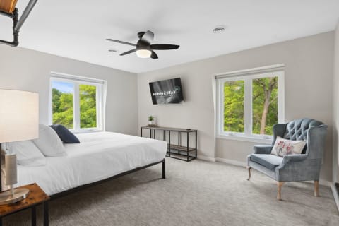 A cozy and modern bedroom featuring a large bed, a television, and green views through the windows.