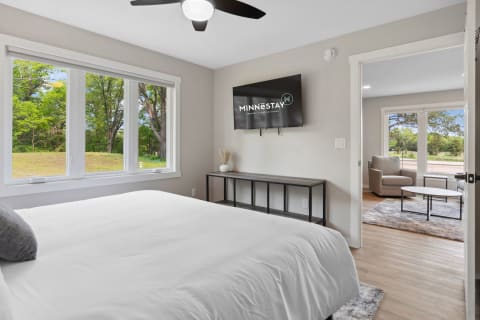 Cozy bedroom featuring a white bed, large windows, and a flat-screen TV.
