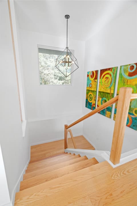 A staircase featuring light wood steps and a geometric pendant light, complemented by colorful abstract wall art.