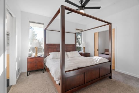Bright and inviting bedroom with a four-poster bed and cozy decor, featuring large windows and carpeted flooring.