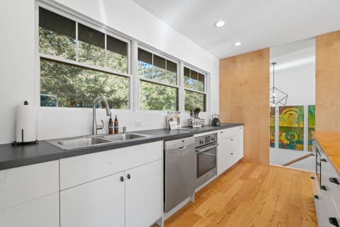 A minimalist kitchen featuring a double sink, stainless steel appliances, and abstract art on the wall.