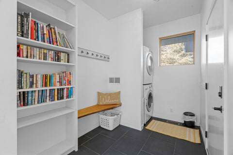 Interior of a modern mudroom featuring a bookshelf, bench, washer, and dryer.