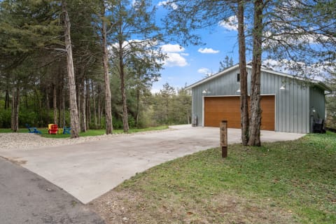 A contemporary garage with a wooden door set among tall trees, featuring colorful Adirondack chairs in the foreground.