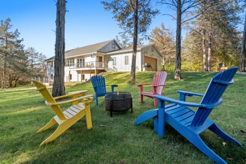 Colorful chairs and fire pit in a backyard with a modern house and clear skies.