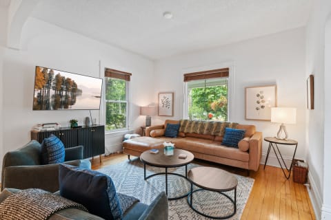 Cozy living room with a leather sofa, coffee table, and large windows, featuring a serene TV landscape.