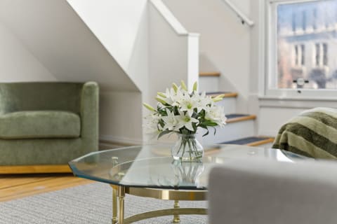 A bright living area with a decorative glass table, white lilies, and soft green seating.