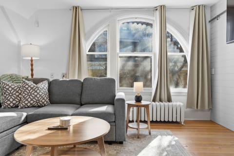 A cozy living room featuring a gray sectional couch, arched windows, and warm wooden accents.