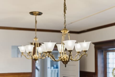 Two brass chandeliers with white glass shades illuminating a dining space.