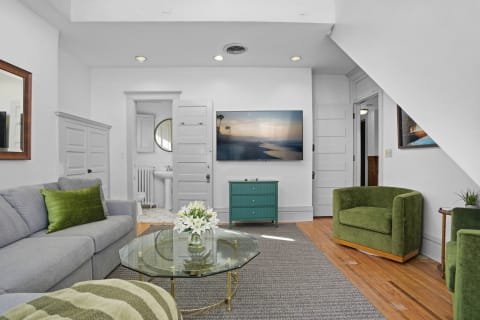Stylish living room featuring a gray sofa, green armchairs, and beach-themed artwork.