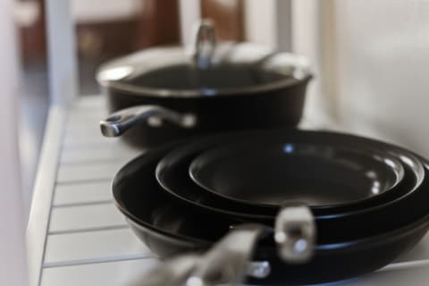 A collection of black cookware, including frying pans and a pot, neatly arranged on a white shelf in a kitchen.