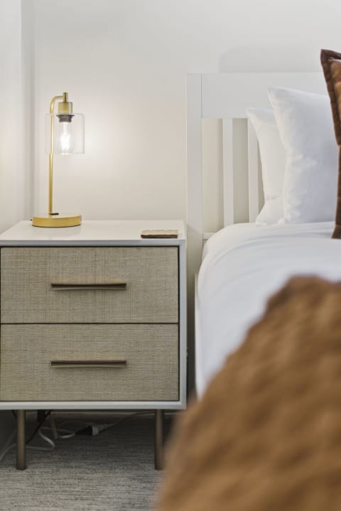 A modern nightstand with textured drawers and a glowing lamp beside a neatly made bed.