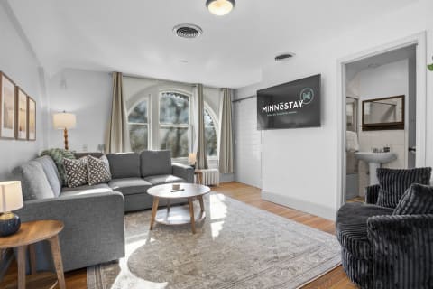 Cozy living space with a grey sofa, large windows, and wooden accents for relaxation.