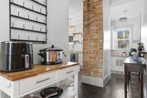 A modern kitchen with brick accent wall, wooden countertop with appliances, and bright windows.