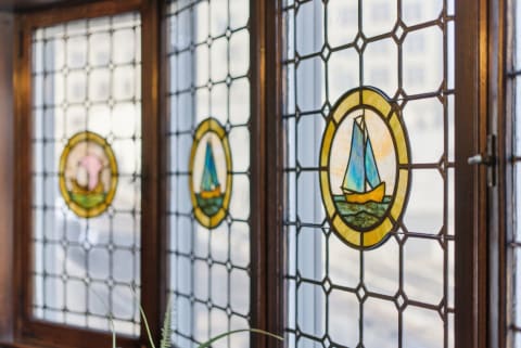 Three stained glass windows with nautical themes, including a pink dolphin and a sailboat, framed in wood.
