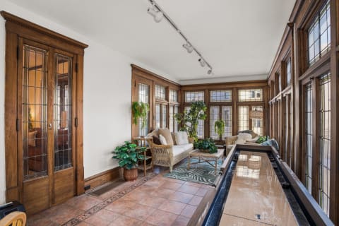 A sunroom featuring wooden accents, cozy seating, and numerous plants, creating a serene atmosphere.