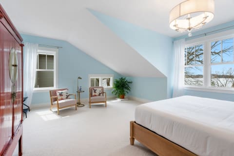 Bright bedroom featuring blue walls, white bedding, and two chairs by the window.