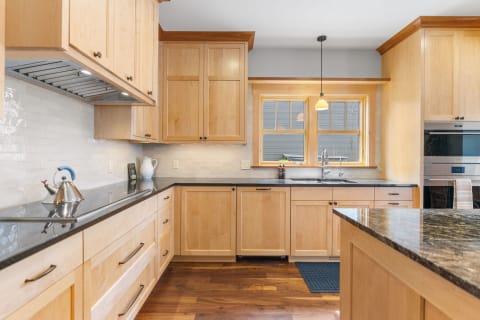 Modern kitchen showcasing wooden cabinets, granite countertop, and natural light from the window.